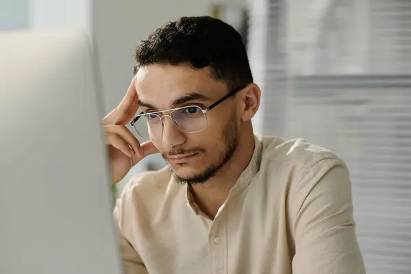 年轻的穆斯林男性白领戴着眼镜 一边看电脑屏幕 一边分析网上数据或观看视频 — 图库照片