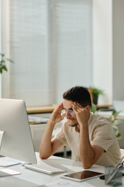 Endişeli erkek ofis çalışanı bilgisayar ekranının önünde oturup sayfayı yüklemeye çalışırken konsantre olmaya çalışıyor.