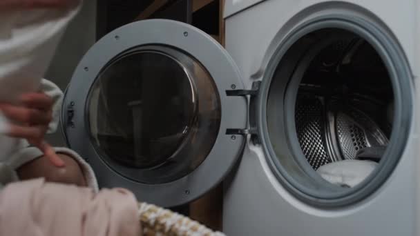 白いバスローブの匿名の若い女性の手のクローズアップショット 洗濯機および閉鎖ドアに荷を積む洗濯のバスケットから汚れた服を取ります — ストック動画