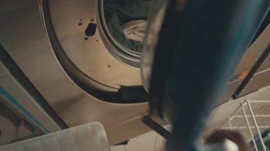 Kimliği belirsiz bir adamın çamaşır makinesine gelip temiz ıslak bezleri çamaşırhanedeki plastik sepete koyarkenki görüntüsü.