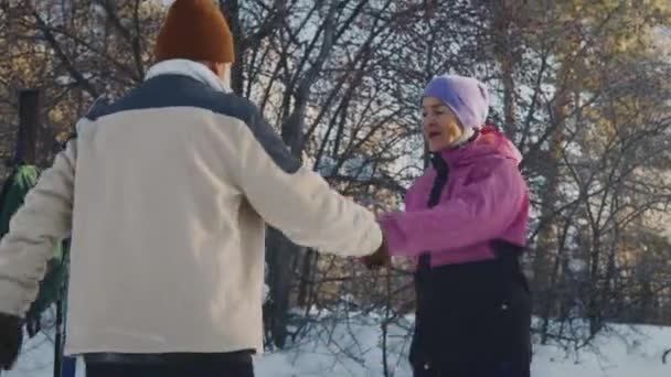ウリー帽子で年配の白人女性を笑顔にする中型傾斜ショット 夫とウォームアップエクササイズを行っている暖かいジャケット スカウト スイングアーム 一緒に森でスキー旅行に行く前に — ストック動画
