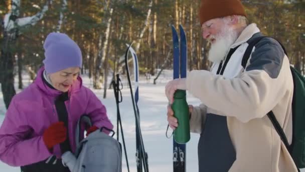 冬日里 白种人男子和女子站在雪地里的滑雪板和杆子旁边 打开背包 拿出热水瓶 一边聊天一边享用热茶 一边休息 — 图库视频影像