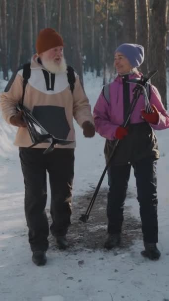 全垂直跟踪拍摄了一对白种人夫妇 穿着温暖的雪衣 穿行在雪地的森林里 带着越野滑雪 男人讲故事 女人惊讶地反应 — 图库视频影像