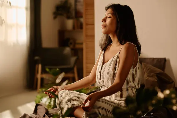 Uzun saçlı, uzun saçlı, yatakta yoga yapan genç ve dingin bir kadın. Sabahları nilüfer çiçeği pozu verip dengesini koruyor.