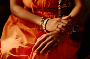 Kırmızı elbiseli, bilezik takmış, serinlerken ya da dinlenirken kameranın karşısında oturan tanınmayan genç bir kadının elleri.