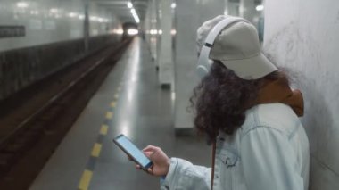 Kafkasyalı genç bir adamın beyaz krom anahtar ekranlı cep telefonuna bakıp metro istasyonunda tek başına tren beklerken görüntülerini kaldır.
