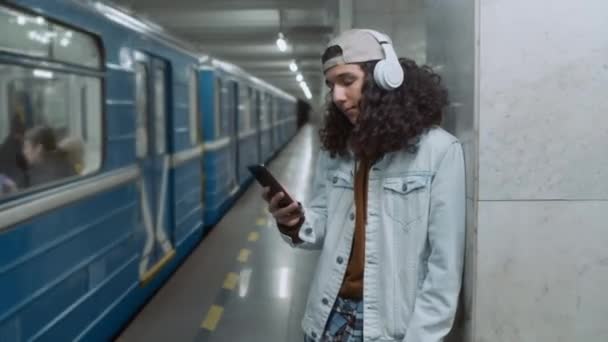 헤드셋에서 음악을 역에서 전화를 지하철 지하철 기차를 기다리는 소년의 동영상 — 비디오