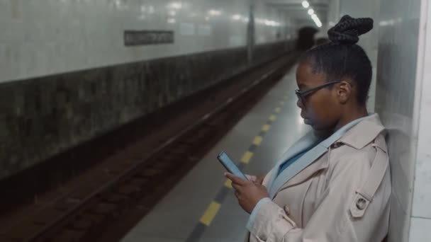 플랫폼에서 그녀의 지하철 기다리는 전화에 메시지를 안경과 트렌치 코트에 비즈니스 — 비디오