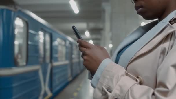 非洲裔美国女通勤者站在地下站台等下一班火车时 戴着眼镜 侧身倾斜 一边用智能手机发短信 — 图库视频影像