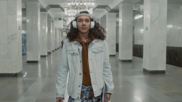 Kulaklıkla Müzik Dinlerken Uzun Koridorda Yürüyen Canlı Kaykaylı Genç Beyaz — Stok video