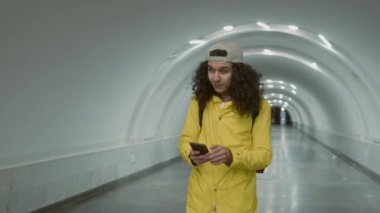 Sarı ceketli beyaz teslimatçının yavaş yavaş izini sürüyorum. Elinde cep telefonuyla tünel boyunca yürürken kırmızı sırt çantasıyla yiyecek getiriyor.