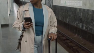Endişeli ve sabırsız görünen bavullu Afrikalı Amerikalı kadının videosu. Cep telefonlarını kontrol ediyor ve metro trenini beklerken geç kalıyor.