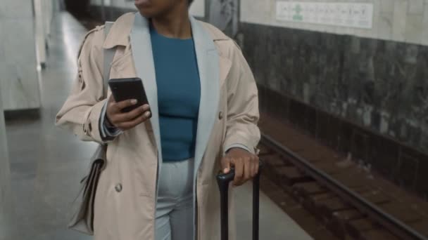 スーツケースを持ったアフリカ系アメリカ人女性のチルト映像は 心配して携帯電話をチェックし 遅刻している間に地下鉄の地下鉄を待っています — ストック動画