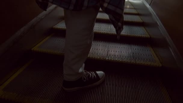 穿着滑板式服装的匿名乘客从自动扶梯下并前往地铁出口的后跟跟踪膝部镜头 — 图库视频影像