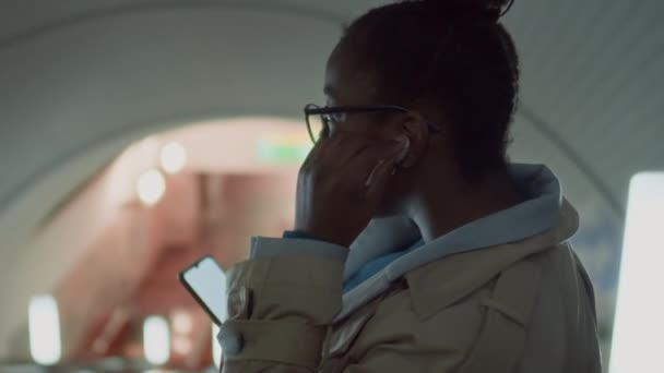 에스컬레이터를 지하철 내려가는 이어폰을 전화를 사용하여 안경에 숙녀의 동영상 — 비디오