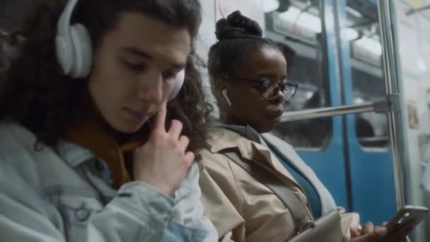 公共地下鉄を移動し ワイヤレスデジタルデバイス ヘッドフォン 携帯電話を使用する多様な男性と女性の乗客のサイド傾斜クローズアップ — ストック動画