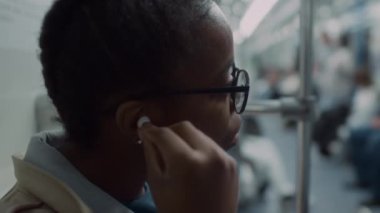 Gözlüklü, metroyla toplu taşıma araçlarıyla seyahat ederken kulaklarına takan Afro-Amerikalı kadın banliyö görevlisi.
