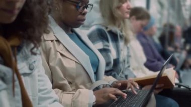 Toplu taşıma araçlarını sürerken bilgisayarla uzaktan çalışan Afrikalı Amerikalı iş kadınının yan eğim görüntüleri.