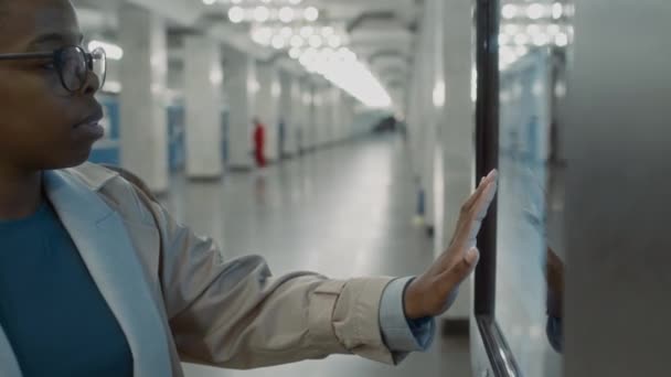 アフリカ系アメリカ人女性観光客が空のプラットフォームに立って地下鉄の地図 地下鉄のスケジュール 列車の到着時間を見ながら一人で移動する映像 — ストック動画