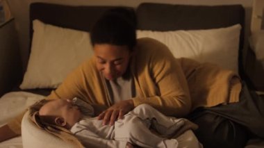 Pijama ve kardiyo giymiş melez bir annenin gece yatakta oturup kozanın içinde uyuyan oğlunu okşaması ve sonra onu öpüp kestirmesi için uzanması.