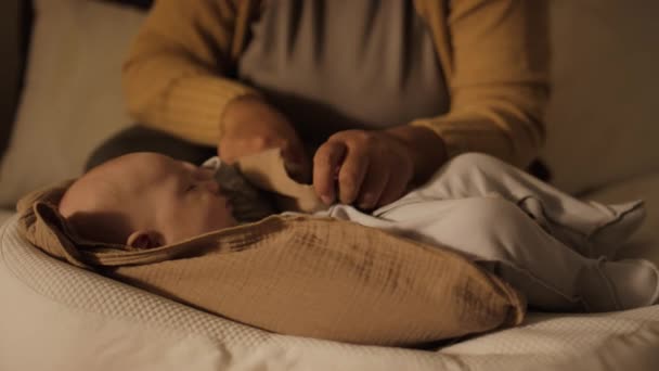 認識できない母親の手のクローズアップショットは コクーンベッドで寝るために新生児を置き 子供の足の下にタッキングし 筋肉シートをまっすぐにする — ストック動画