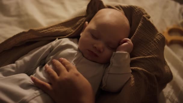 コクーンポッドで寝ているボディスーツを着た新生児の男の子のトップクローズアップショットと 認識できない母親の手は優しく頭と頬に彼をストローク — ストック動画