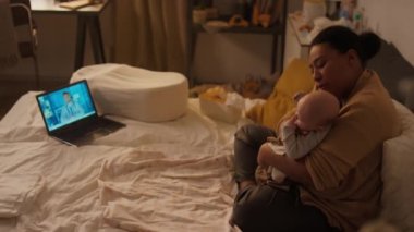 Tam bir çift ırklı anne çocuğu kucağına alıp kucaklıyor ve dizüstü bilgisayarında teletıp danışmanlık yaparken doktorların tavsiyelerini dinliyor.