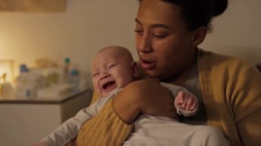 Afrika kökenli Amerikalı bir annenin burun piercingli, mızmız, ağlayan bir bebeği kucağında sallarken, sarılırken ve onu sakinleştirmeye çalışırken, doğum izni sırasında oğluyla ilgilenirken.