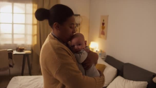 ヒスパニック系またはアフリカ系アメリカ人の母親がTシャツとカードリーを着て かわいい赤ん坊の息子を抱え 部屋を歩き回り 昼間の睡眠のために彼を落ち着かせるためにロッキング — ストック動画