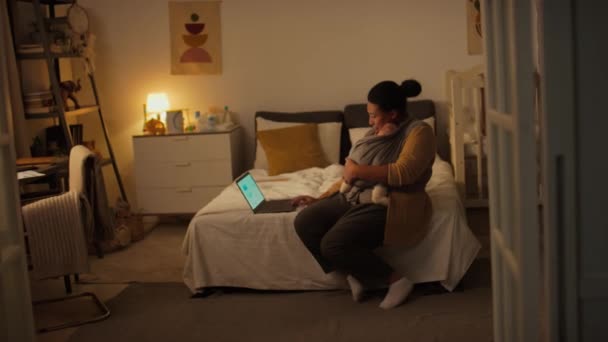 自宅でベッドに座って 昼間の睡眠中にラップトップでビジネスプレゼンテーションに取り組む赤ちゃんとアフリカ系アメリカ人の母親のフルショット — ストック動画