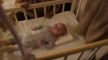 Bebek arabasının altında beşikte yatmış, tekmeliyor, gurulduyor, gevezelik ediyor ve tanınamayan anne ya da dadının yanında oturan üç aylık mutlu bir erkek bebek.