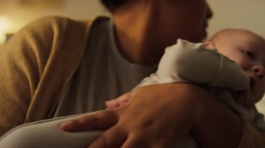 Annesinin kollarında dört aylık mızmız bir çocuğun yakın plan fotoğrafı. Sallanıyor, sarılıyor, ıslak dudaklarını peçeteyle siliyor ve diş çıkarırken onu sakinleştiriyor.