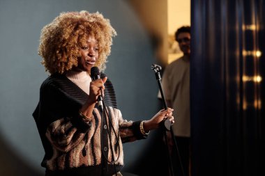 Sahnedeki performans sırasında mikrofonla konuşan genç Afrikalı Amerikalı kadın sunucu veya komedyen.