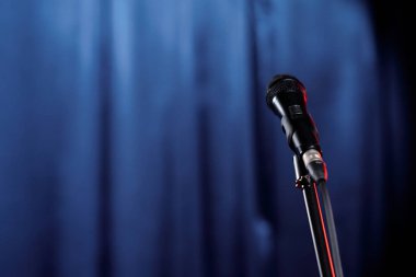 Mikrofon, komedyen ya da akşam şovuna katılan kişinin mavi sahne perdelerine karşı performansı için hazır.