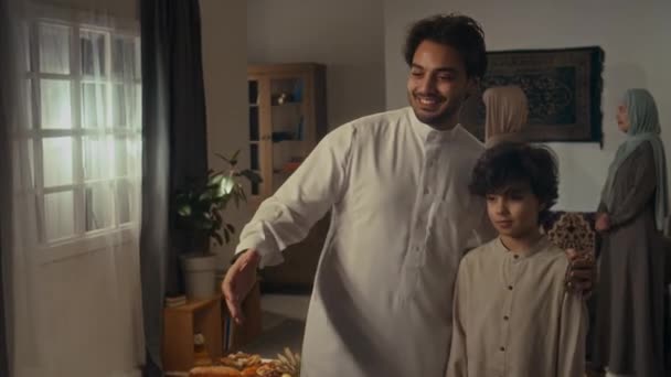 中镜头中 两个男人和他的儿子都出现在电视上 向前来与家人一起庆祝开斋节的身份不明的男性亲属致意 — 图库视频影像