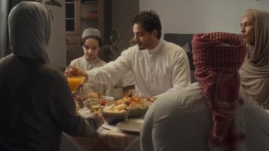 Büyük İslami ailenin evde bayram yemeği yediği arka görüntüler. Genç adam bardaklara portakal suyu dolduruyor ve akrabalara servis yapıyor.