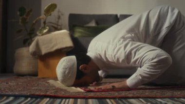 Evdeki dua haritasında Allah 'a secde ederken başlık takmış Müslüman bir adamın yan görüntüsü.