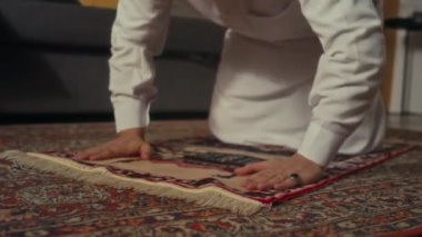 Beyaz, geleneksel giyinmiş, dindar, sakallı bir adamın evde halıda namaz kılarken birkaç kez sujud pozisyonu aldığı zemin kattaki görüntüler.