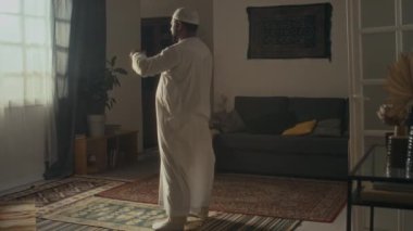 Beyaz şapkalı kimliği belirsiz dindar bir adamın Ruku 'yu yaparken ve evde dua minderinde Allah' a şükranlarını sunarken çekilmiş geniş bir görüntüsü.