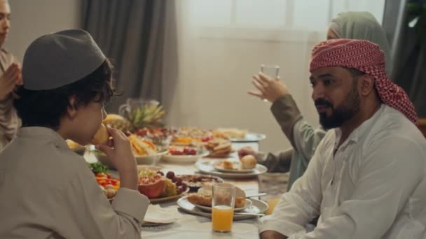 ターバンのBiracialarded父親のサイドハンドヘルド映像は 彼の息子や甥が自宅でイードアルフィトルのイスラム教徒の休日を祝っている間 お祝いのテーブルに近くに座って話しています — ストック動画