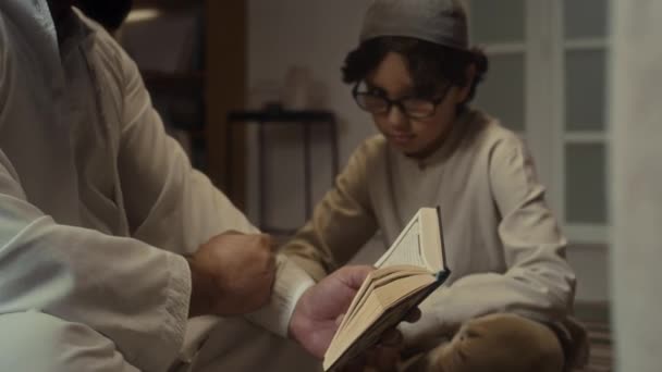 白いクルタの白いクルタのひげの父親の横の傾きの映像は コーランを読んで 常にうなずく小さな息子にその規則と原則を説明しています — ストック動画