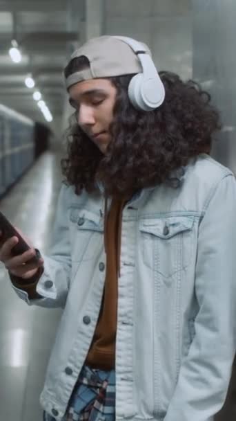 헤드셋에서 음악을 역에서 전화를보고있는 지하철 지하철 기차를 기다리는 잘생긴 소년의 — 비디오