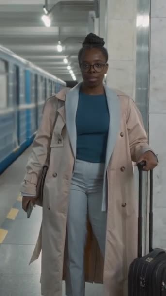 身着眼镜 提着手提箱的非洲裔美国女旅行者的垂直肖像 接近离开蓝色的地下铁列车 看着镜头 — 图库视频影像