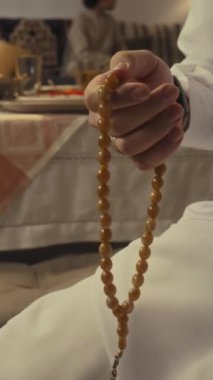 Bayram günü evde namaz kılarken geleneksel giysiler içinde Tasbih kullanan genç bir Arap 'ın dikey eğim görüntüleri.