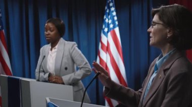 Genç Afrikalı Amerikalı kadın muhalefet adayının ekonomik politikalar konusunda rakibini eleştirdiği orta boy bir fotoğraf ve seçim tartışmalarında çelişen ve karşı çıkan olgun beyaz kadın senatör.