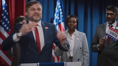 Demokratik parti kongresinde sahnede konuşan, dinleyicilerle iletişim kuran, cömert vaatlerde bulunan enerjik gülümseyen beyaz erkek adayın orta boy görüntüleri.
