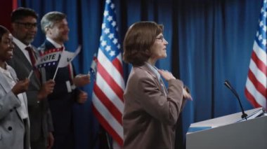 Cumhuriyetçi ya da Demokrat Parti 'den Beyaz kadın başkan adayının sahnede podyumda durup, salondaki katılımcılara coşkulu bir konuşma yaptığı orta yaş görüntüler.