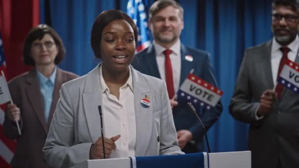 一位热情洋溢的年轻非洲裔美国女总统候选人站在讲台上 为美国选举发表了充满活力的政治宣言 背景各异的团队 — 图库视频影像