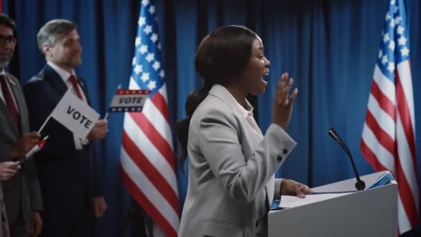 トリビューンに立つ民主党の大統領または市長のための若いアフリカ系アメリカ人女性候補者の中央側の映像と ホールで公開する精力的な政策演説 — ストック動画