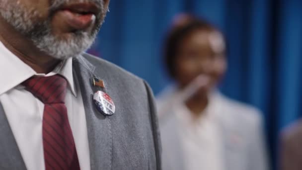 灰色のスーツ 白いシャツ 赤いネクタイ 投票と米国の旗バッジで認識できないアジア人男性の上部ボディのクローズアップショット 民主党または共和党大会の選挙 — ストック動画